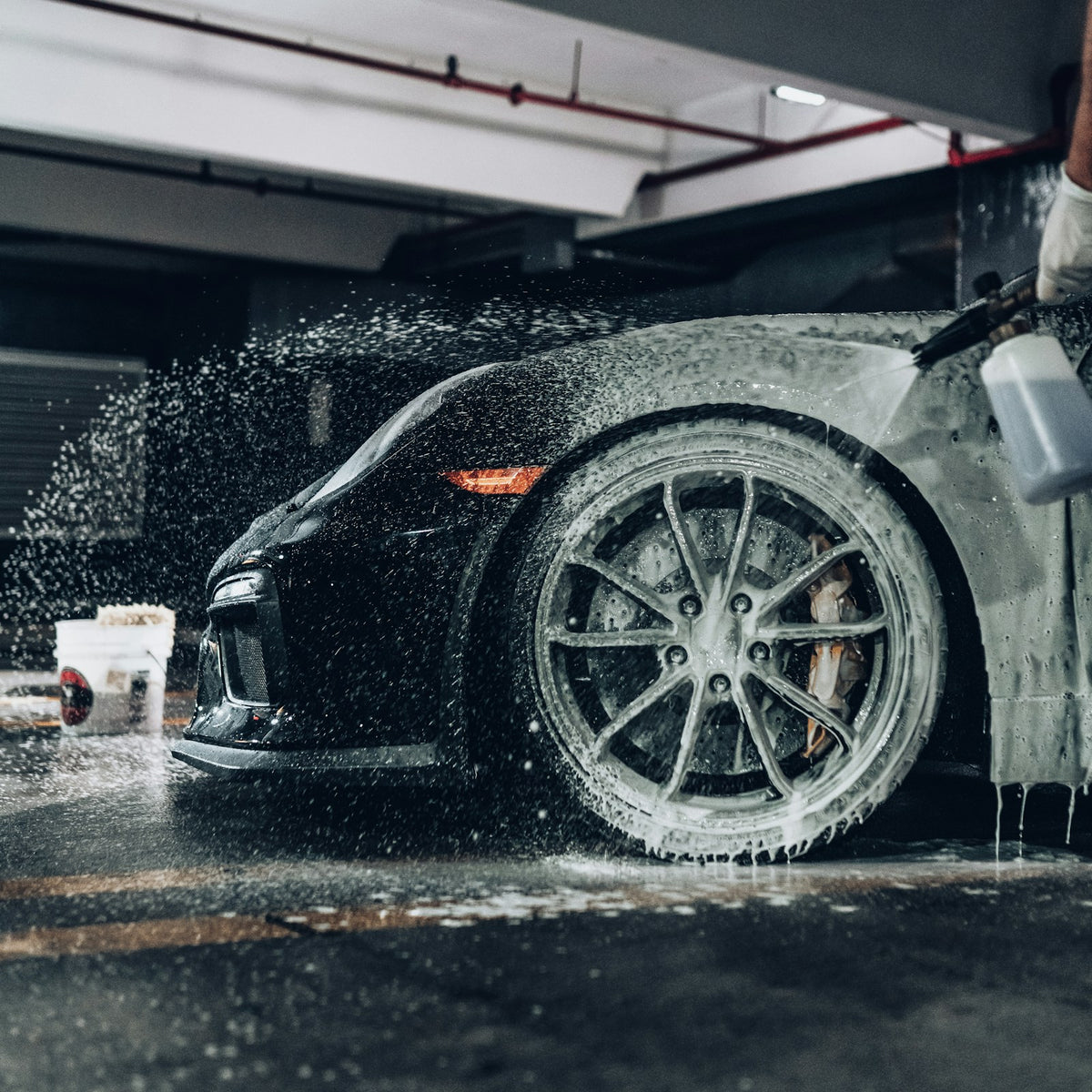 Foam washing a black sports car in a garage, photographed by Andre Tan